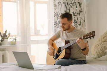 Man plays an acoustic guitar in an online lesson. Hobby a musician. - obrazy, fototapety, plakaty