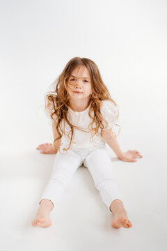 beautiful little girl with long hair in white clothes sits on the floor.