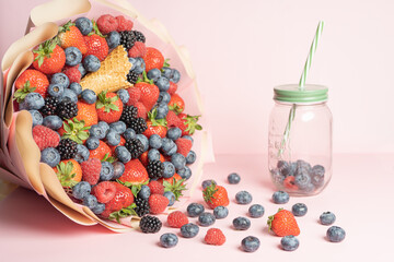 Edible bouquet of fresh berries, blueberries, raspberries, strawberries, hedgehog on a pink background with scattered berries and a jar for smoothies. View from the top .Close-up 
