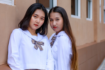Cute and young girls wearing Japanese, Korean style schoolgirl uniform pose to camera together with fun and happy in front of school building. Close friends in college concept