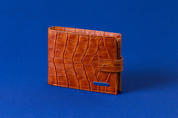 Brown reptile leather wallet on blue fabric background. Fashion and shopping concept