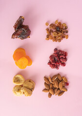 Healthy dried fruits: almonds, figs, raisins, cranberries, dates and apricots on a pastel pink background. Flat lay minimal arrangement.