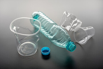 Disposal of plastic dishes. Used glasses and bottle on a gray background. Ecology concept.
