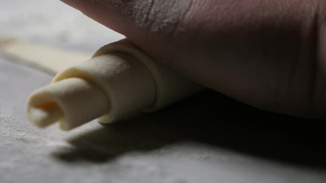 Worker hands twisting up a dought sheet to shape in a croissant at a bakery plant 