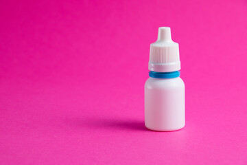 White bottle with nose or eye drops on a pink paper background. Medicine on background with copy space.
