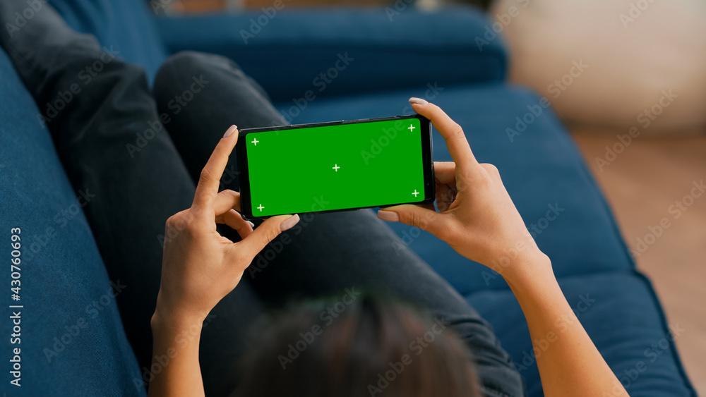 Poster freelancer sitting on sofa while looking at movies using phone in horizontal mode with mock up green