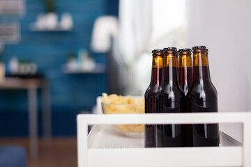 Close up of dark beer bottle in elegant apartment. Modern living room with nobody in with blue furniture and walls, beautiful decorated. Pretty simple decor of apartment. Elegant retro decoration