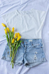 Women clothing spring flat lay with blue jeans shorts, white shirt, sneakers and yellow tulips, fashion blogger content, copy space