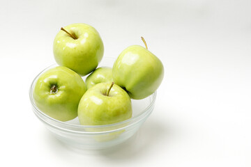 green apples in a transparent bowl on a white background
