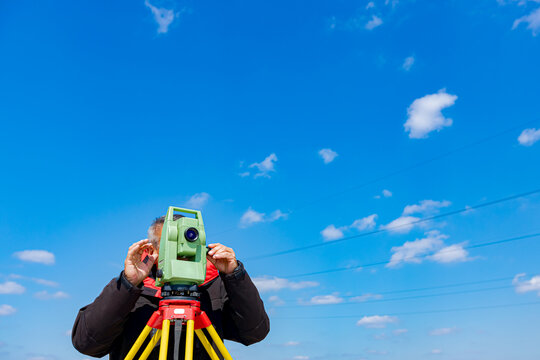Civil engineer, geodesist is working with total station on a building site, blue sky in background
