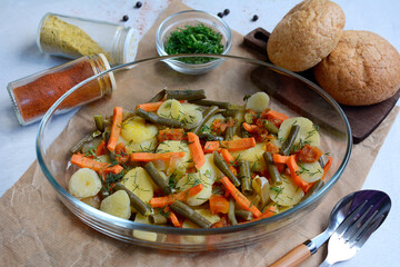 Close-up of vegetables baked in the oven in a glass bowl, bread, spices on a light background.