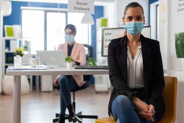 Entreprene portrait looking at camera with face mask as safety precaution keepig social distancing from coworkes during clobal outbreak with covid-19. Business employee working behind separation