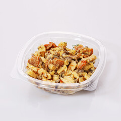 Salad of carrots, meat, cheese and sauce in a transparent plastic bowl on a white background.