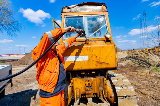Hand holding handle fuel nozzle to refuel, petrol is pouring into the tank of an industrial mechanization