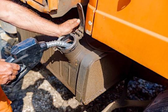Hand holding handle fuel nozzle to refuel, petrol is pouring into the tank of an industrial mechanization