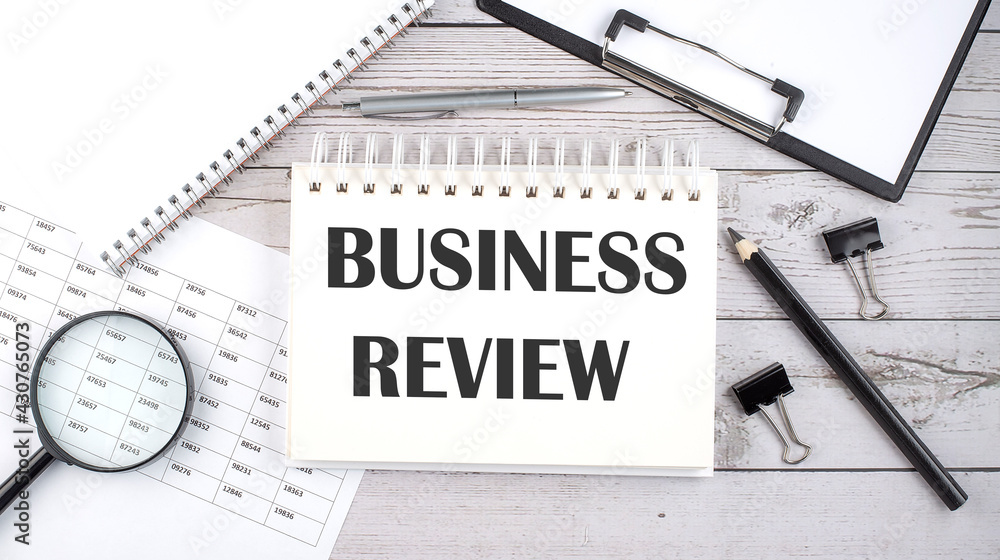 Poster notepad with text business review with a pen,office tools and graphs on the desktop.