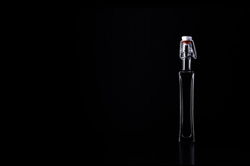 Small slim glass bottle of liquor isolated on black background