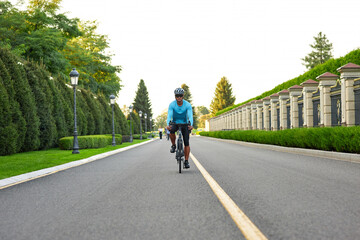 Full length shot of professional road bicycle racer in sportswear and protective helmet training in the park