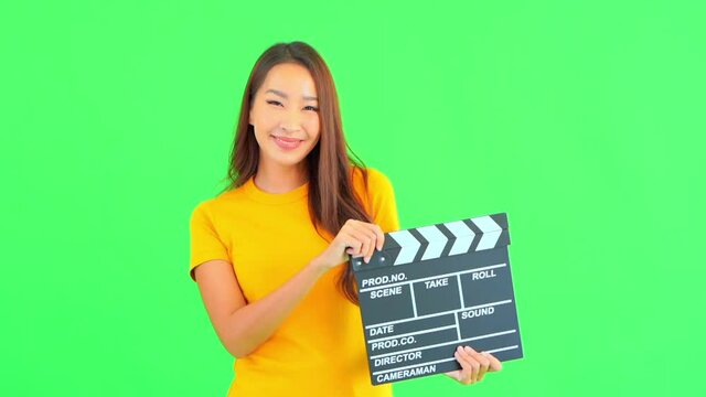 Smiling Asian woman with yellow t-shirt holds clapperboard. Green screen choma key in background