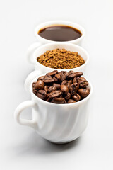 Three white cups with coffee beans, ground coffee and coffee drink