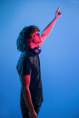 Fototapeta na wymiar With headphones. Young beautiful man with curly hair is indoors in the studio with neon lighting