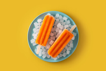 Orange popsicles on blue plate on yellow background