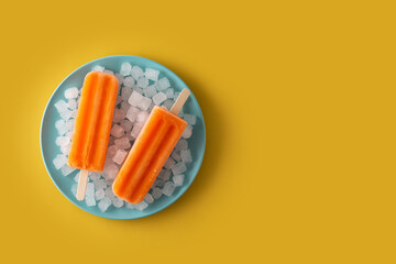 Orange popsicles on blue plate on yellow background
