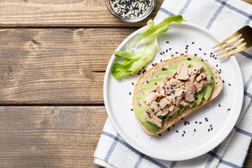Avocado, canned tuna toast on wooden table background. Healthy food, avocado open sandwich for breakfast or lunch. Flat lay, top view, copy space