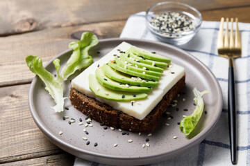 Rye bread toast with goat cheese and avocado on wooden table background. Healthy avocado open sandwich for breakfast or lunch.