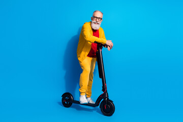 Full size photo of positive person standing on scooter look camera toothy smile isolated on blue color background © deagreez