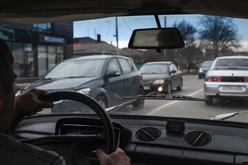 The driver in the car is driving in the city and looks at the road and cars moving in the oncoming lane through the windshield, a first-person view.