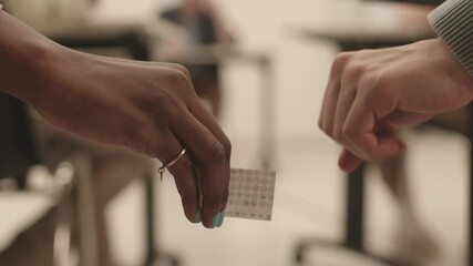 Locked-down of hands of two unrecognizable students passing over cheat sheet for exam on blurred background