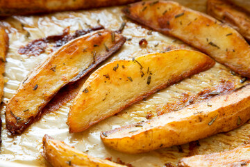 Homemade Rosemary Potato Wedges on a baking tray, side view. Close-up.