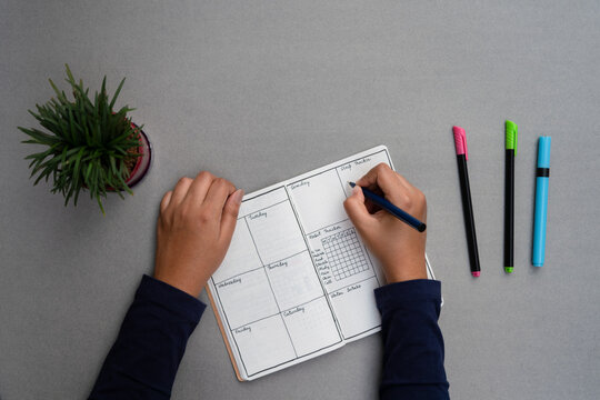 Setting up a bullet journal for mental well being and personal development. Weekly planner set up on a minimal grey table top, with sketch pens and a green house plant