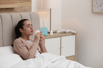 Sick young woman with napkins and nasal spray in bed at home