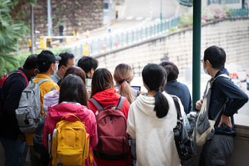 university or college students with face mask and school bag gather together to listen to professor or teacher about field test during trip in Hong Kong, aid of computer. Small group teaching