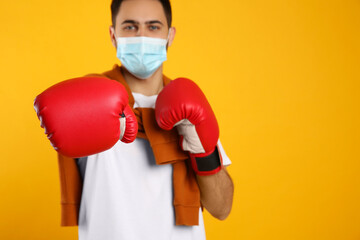 Man with protective mask and boxing gloves on yellow background, space for text. Strong immunity concept