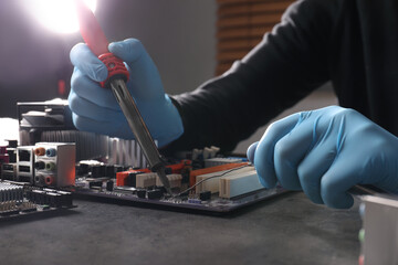 Technician repairing electronic circuit board with soldering iron at table, closeup