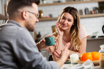 Beautiful young girl enjoying in breakfast with her boyfriend. Loving couple drinking coffee in the kitchen