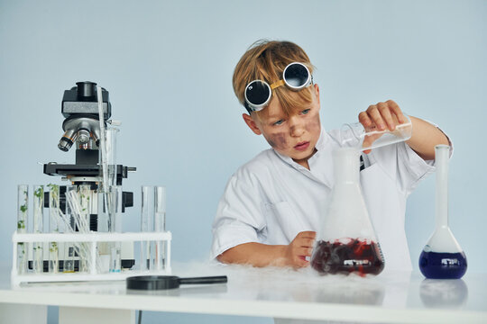 Little boy in coat playing a scientist in lab by using equipment