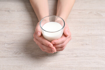 Woman holding glass of milk at white wooden table, closeup