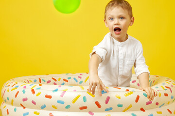 A small smiling boy plays in a dry pool on a yellow background. A child throws a green plastic ball
