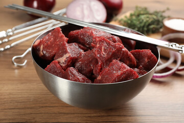 Metal skewers and bowl with raw meat on wooden table
