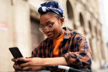 Happy young woman riding bicycle in the city. Woman with curly hair using the phone.