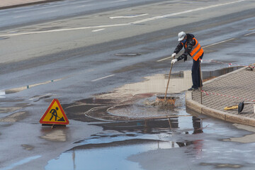 Uralsk, Kazakhstan (Qazaqstan), 08/01/2019: a man cleans a puddle with a shovel after rain, improperly designed road, bad road, cleaning in the city