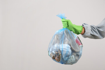 Woman holding full garbage bag on light background, closeup. Space for text