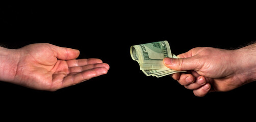 Person hand gives dollars and other human hand takes on black isolated background. The idea of...