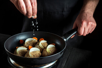 Cooking cutlets on grill pan by chef or cook hands on black background for copy space text restaurant menu. The chef adds salt