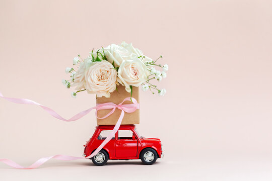 Red car with a gift box of roses flowers on the roof. Holiday concept, flower delivery.