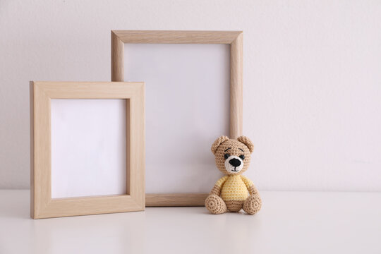 Empty photo frames and toy bear on table near white wall. Space for design